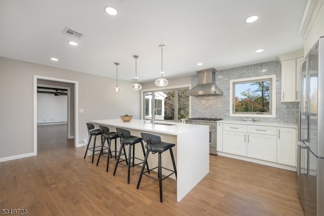 kitchen featuring wall chimney exhaust hood, white cabinets, hanging light fixtures, and a kitchen island with sink