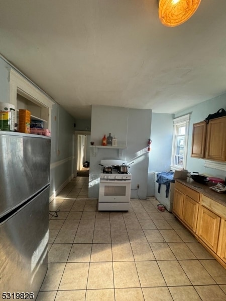 kitchen with light tile patterned floors, white gas stove, and stainless steel refrigerator