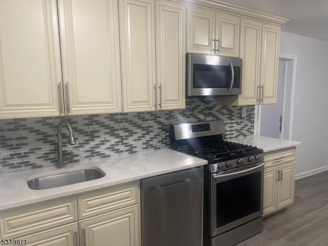 kitchen with cream cabinets, sink, backsplash, stainless steel appliances, and hardwood / wood-style flooring