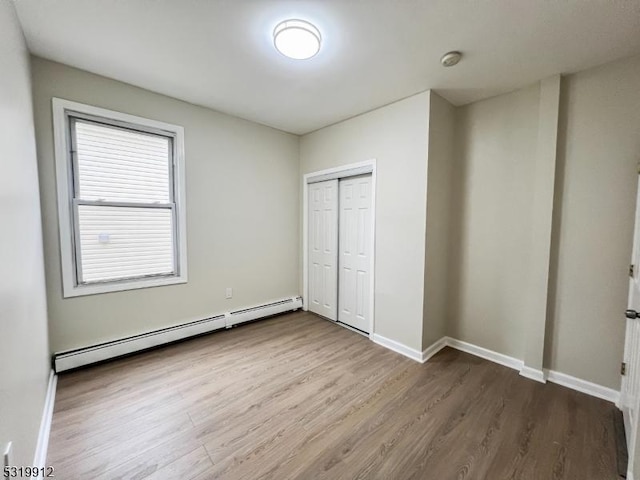 unfurnished bedroom with a baseboard radiator, dark wood-style flooring, baseboards, and a closet