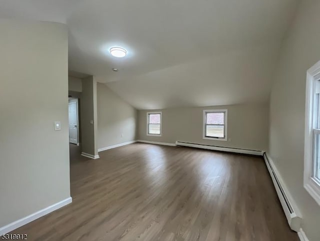additional living space featuring baseboard heating, vaulted ceiling, wood finished floors, and baseboards