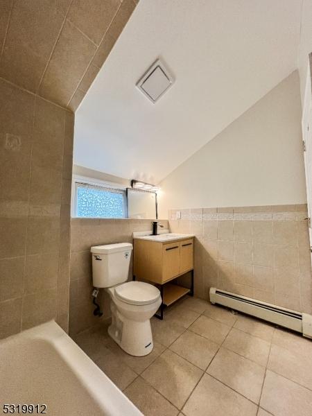 full bathroom with tile walls, a baseboard radiator, lofted ceiling, toilet, and tile patterned flooring
