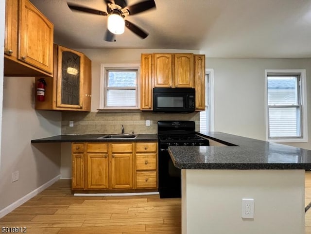 kitchen featuring black appliances, a sink, dark countertops, light wood finished floors, and a ceiling fan