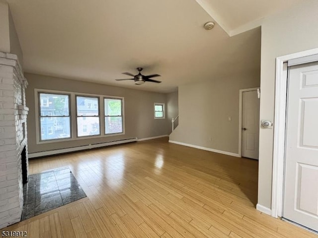 spare room featuring baseboard heating, a ceiling fan, a brick fireplace, baseboards, and light wood-type flooring