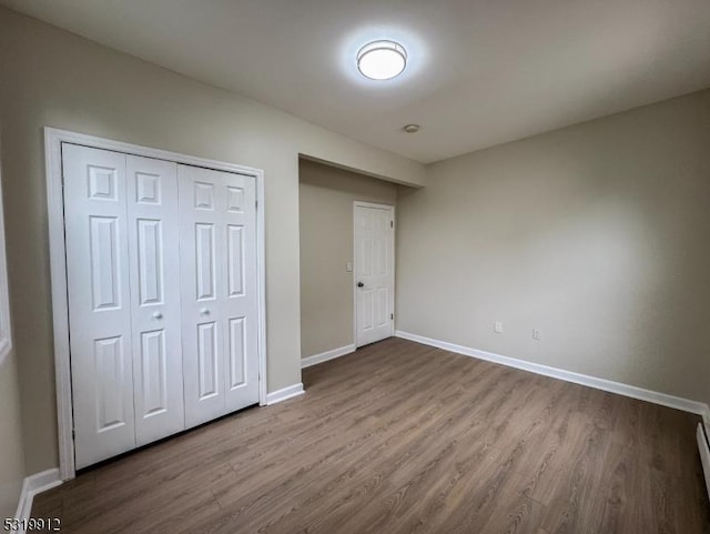unfurnished bedroom featuring dark wood-style floors, baseboards, a closet, and a baseboard heating unit