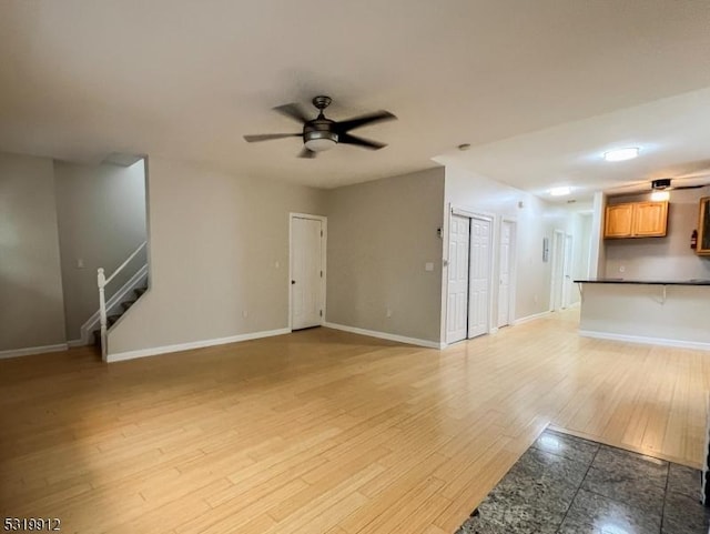 unfurnished living room with baseboards, ceiling fan, stairway, and light wood-style flooring