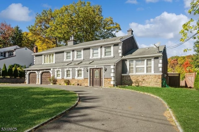 view of front of property featuring a chimney, driveway, stone siding, fence, and a front yard