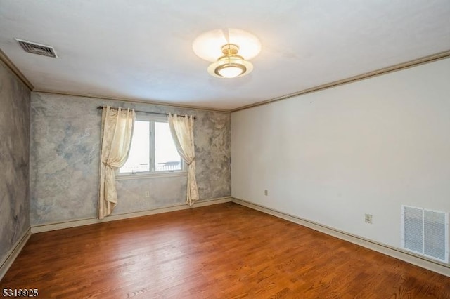 empty room with baseboards, wood finished floors, visible vents, and crown molding