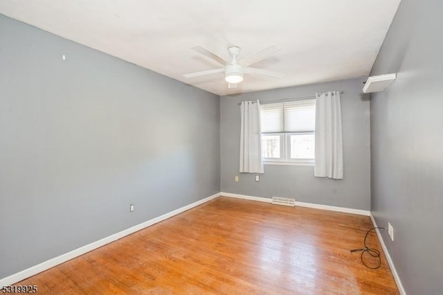 spare room with wood finished floors, visible vents, a ceiling fan, and baseboards