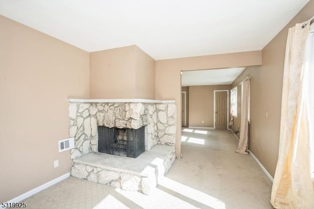 unfurnished living room with baseboards, a stone fireplace, visible vents, and carpet