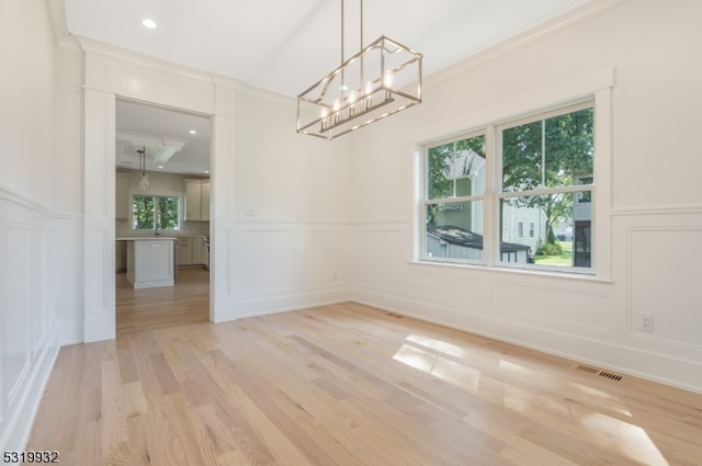 unfurnished dining area featuring an inviting chandelier, ornamental molding, and light wood-type flooring