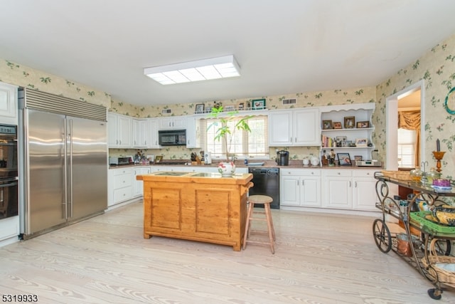 kitchen featuring black appliances, white cabinetry, light hardwood / wood-style floors, and a breakfast bar