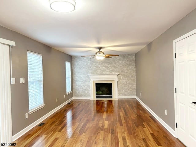 unfurnished living room with brick wall, hardwood / wood-style floors, a large fireplace, and ceiling fan