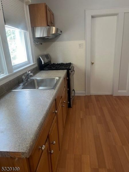 kitchen featuring stainless steel gas stove, light wood-type flooring, sink, and range hood