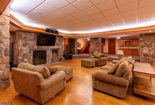 cinema with a drop ceiling, a stone fireplace, a tray ceiling, and light wood-type flooring