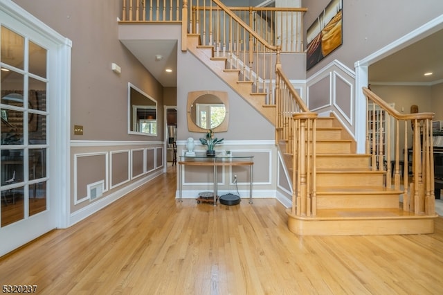 stairway with a towering ceiling, ornamental molding, and hardwood / wood-style floors