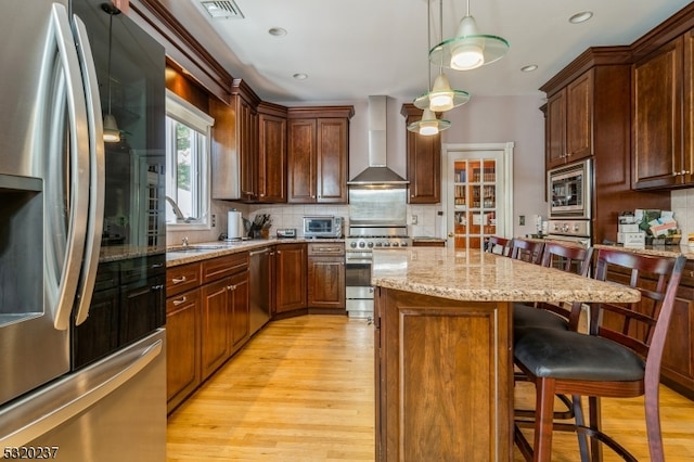 kitchen with wall chimney exhaust hood, appliances with stainless steel finishes, a kitchen island, pendant lighting, and backsplash