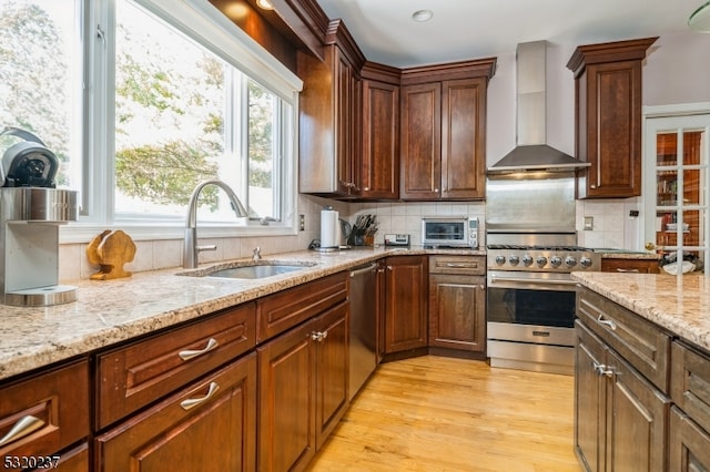 kitchen featuring light stone counters, stainless steel appliances, sink, and wall chimney range hood