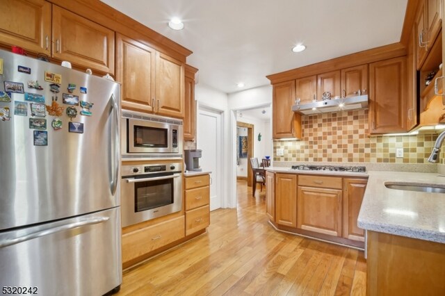 kitchen with tasteful backsplash, sink, light wood-type flooring, stainless steel appliances, and light stone counters