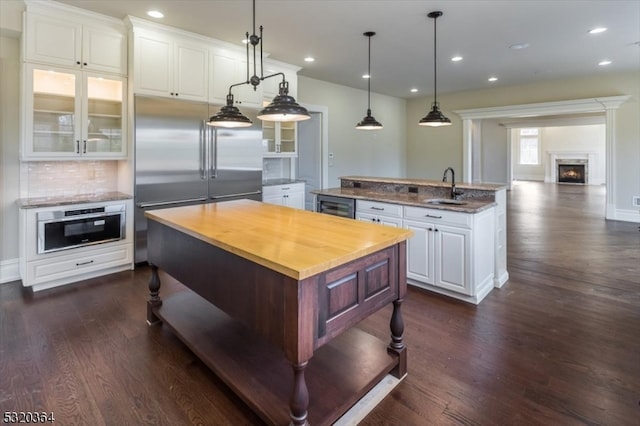 kitchen with butcher block counters, a kitchen island, white cabinetry, appliances with stainless steel finishes, and hanging light fixtures