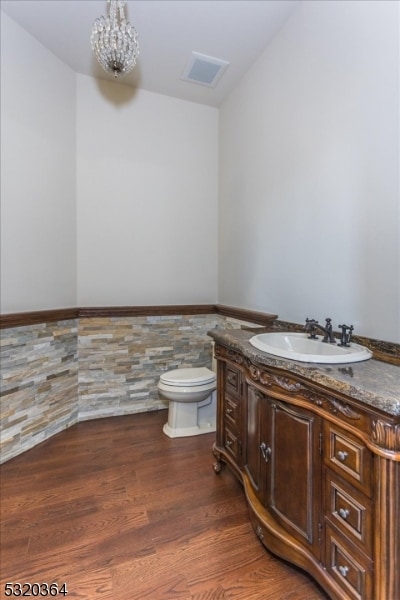 bathroom with wood-type flooring, toilet, tile walls, a notable chandelier, and vanity