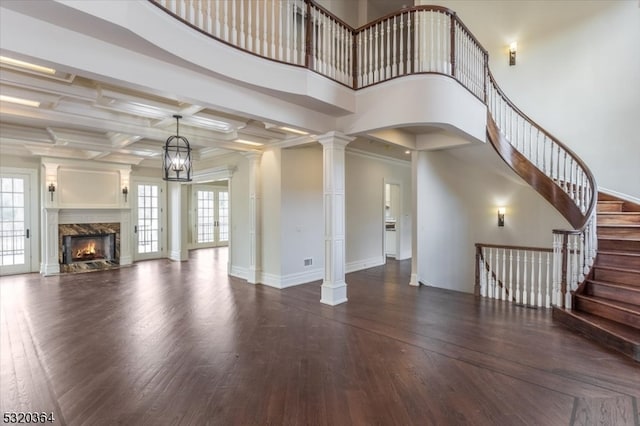 unfurnished living room with ornate columns, dark hardwood / wood-style flooring, a premium fireplace, coffered ceiling, and beamed ceiling