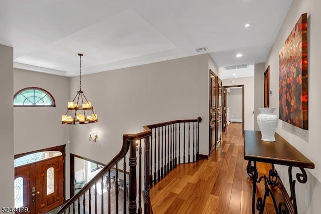 hallway with light hardwood / wood-style flooring, a notable chandelier, and a tray ceiling