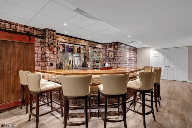 bar with sink, a barn door, a paneled ceiling, wooden walls, and light hardwood / wood-style flooring