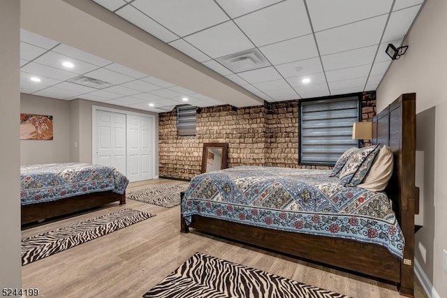 bedroom featuring a drop ceiling, a closet, brick wall, and light wood-type flooring