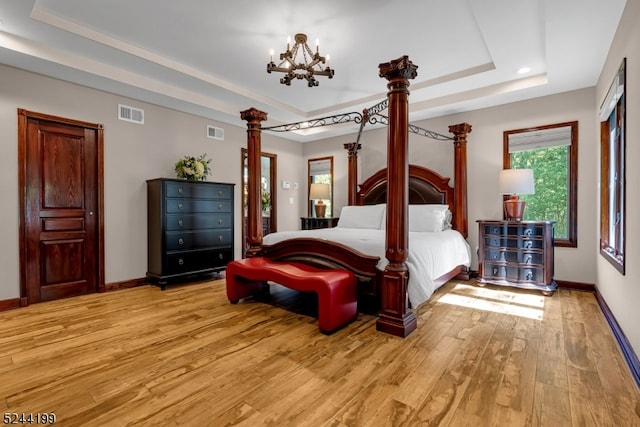 bedroom with an inviting chandelier, light wood-type flooring, and a raised ceiling