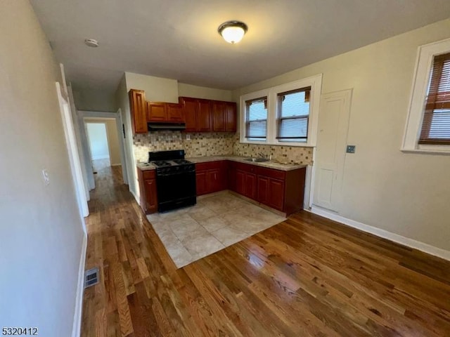 kitchen with black gas range, sink, light wood-type flooring, and backsplash