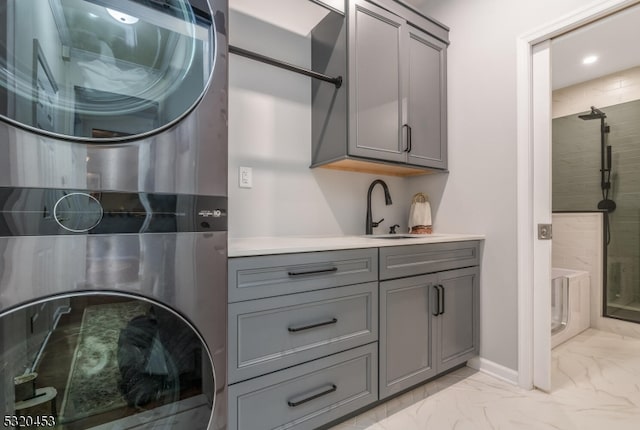 clothes washing area featuring stacked washer and clothes dryer, cabinets, and sink