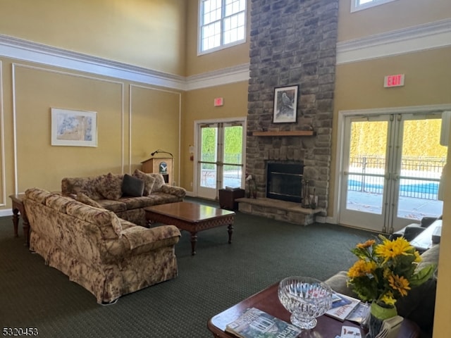 carpeted living room featuring a stone fireplace, crown molding, and a towering ceiling