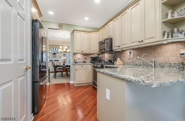 kitchen featuring light stone counters, appliances with stainless steel finishes, a notable chandelier, hardwood / wood-style floors, and sink