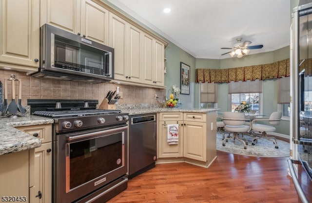 kitchen with light hardwood / wood-style floors, light stone counters, appliances with stainless steel finishes, crown molding, and cream cabinetry