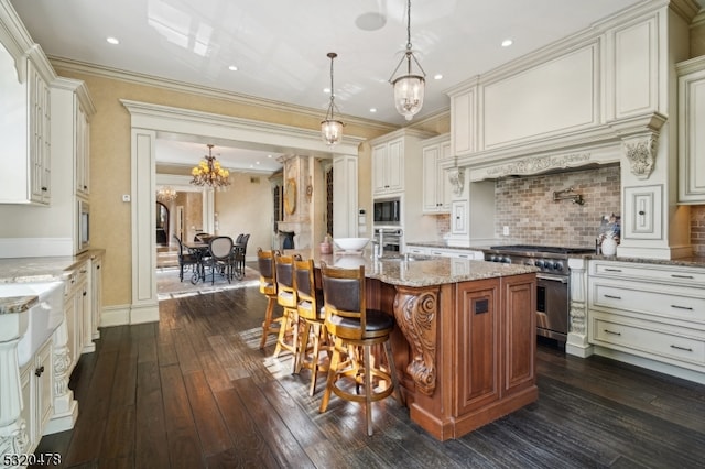 kitchen featuring appliances with stainless steel finishes, decorative light fixtures, light stone counters, dark hardwood / wood-style floors, and a kitchen island with sink