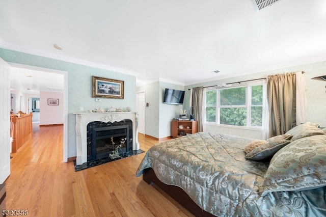 bedroom with ornamental molding, light hardwood / wood-style flooring, and a high end fireplace