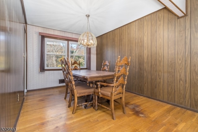 dining area featuring wood walls, light hardwood / wood-style floors, and a chandelier