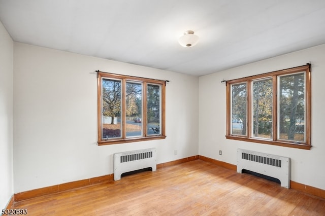 unfurnished room featuring radiator heating unit and light hardwood / wood-style flooring