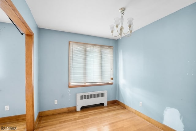 spare room with a chandelier, radiator heating unit, and light wood-type flooring