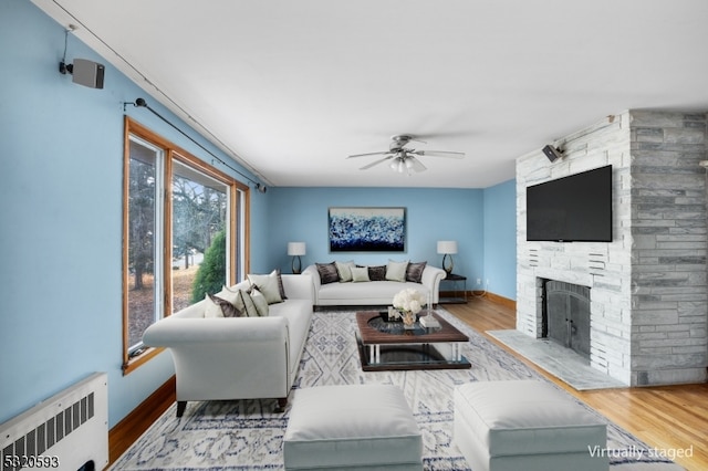 living room featuring a stone fireplace, radiator heating unit, wood-type flooring, and ceiling fan