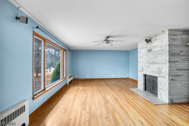 unfurnished living room with ceiling fan, radiator, wood-type flooring, and a stone fireplace