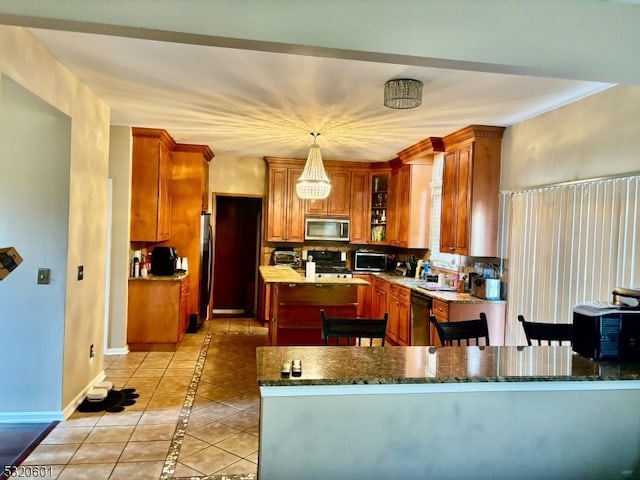 kitchen featuring kitchen peninsula, stainless steel appliances, dark stone countertops, pendant lighting, and light tile patterned floors