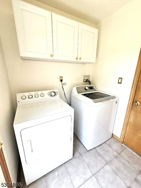 washroom featuring washing machine and dryer, light tile patterned floors, and cabinets