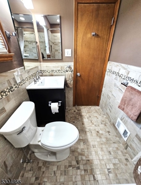 bathroom featuring toilet, vanity, and tile walls