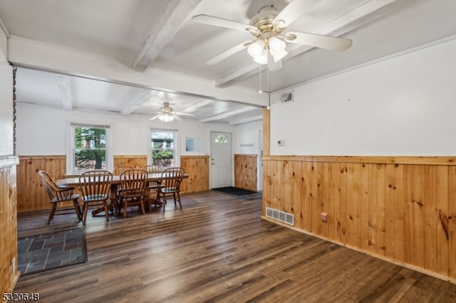 dining room with dark wood-type flooring, ceiling fan, wood walls, and beamed ceiling