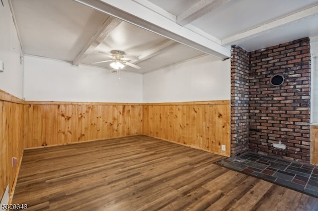 empty room featuring beamed ceiling, ceiling fan, dark hardwood / wood-style floors, and wood walls