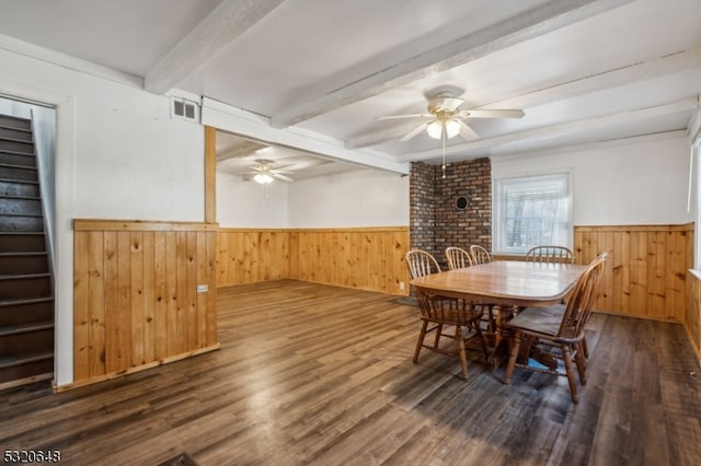 dining room with wood walls, beamed ceiling, ceiling fan, and dark hardwood / wood-style flooring