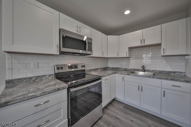 kitchen with stainless steel appliances, backsplash, sink, light wood-type flooring, and white cabinetry