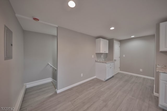 kitchen with white cabinets, light stone countertops, electric panel, and light wood-type flooring